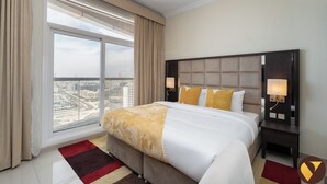 A hotel room with a large bed, a nightstand, a lamp, and a view of the city through a large window. - Vogue | Siraj Tower Arjan near Miracle Garden (Dubai)
