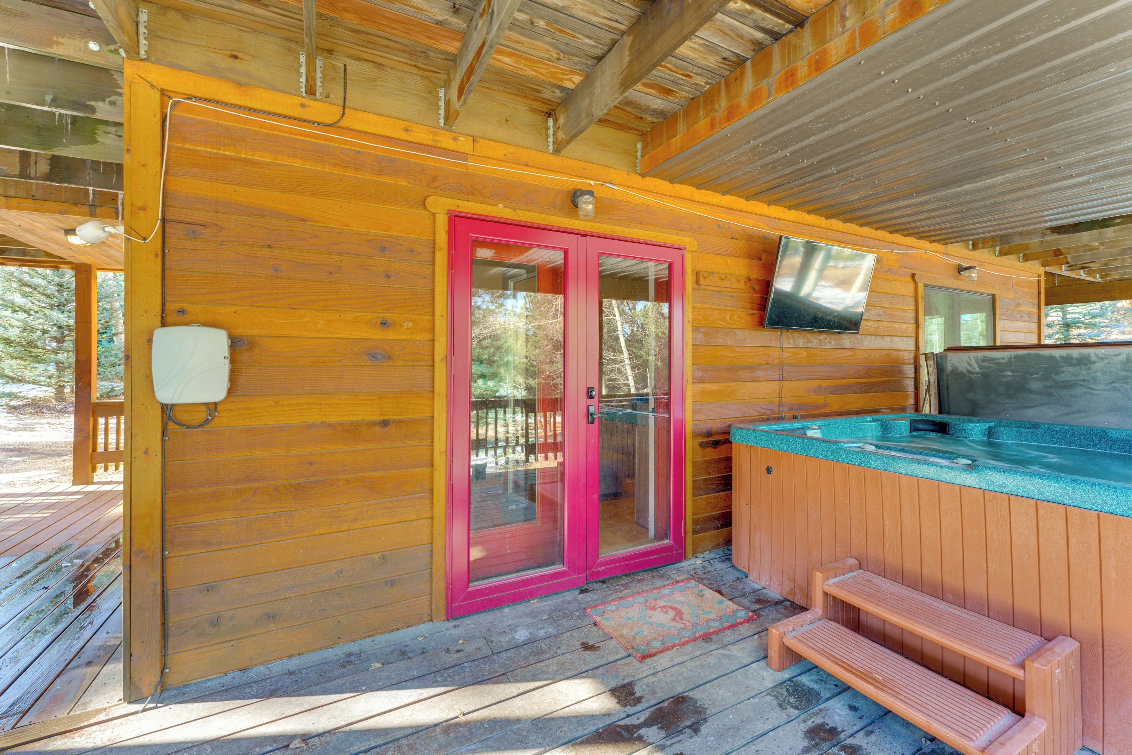 A wooden cabin with a hot tub, a pink door, and a television mounted on the wall.
