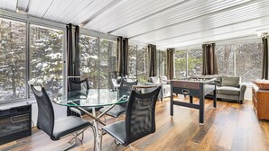 Ein modernes Zimmer mit Glastisch, Stühlen, einem Kicker und Blick auf verschneite Bäume durch große Fenster.