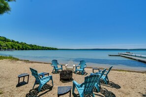 Una playa con sillas y una mesa, un muelle y un lago.