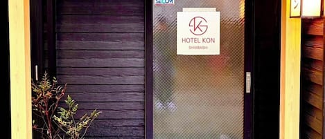 A wooden entrance with a black door, a sign for Hotel Kon, and a small potted plant.