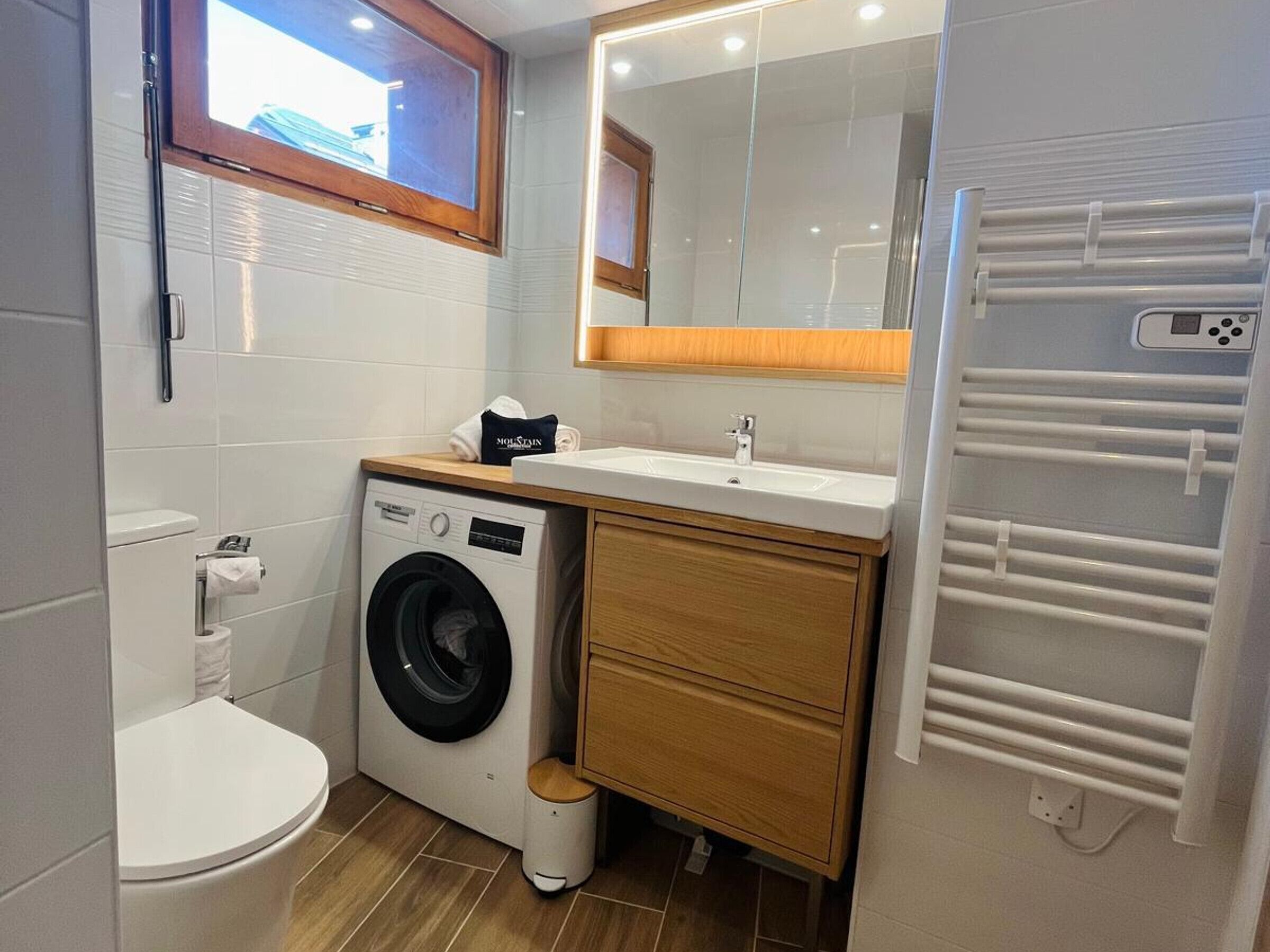 Een kleine badkamer met een wasmachine, toilet en een wastafel met spiegel erboven.