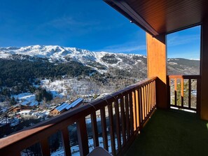 Een balkon met uitzicht op besneeuwde bergen en een dorp daaronder.