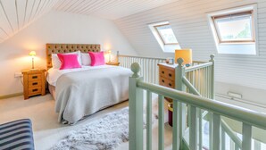 A bedroom with a large bed, two bedside lamps, a fluffy rug, and a wooden nightstand. - Cherry Cottage  Luxury for Couples, Private Use of Indoor Heated Swimming Pool (Faversham)