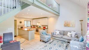 A modern living room with a grey sofa, patterned armchairs, a glass coffee table, and a kitchen in the background. - Cherry Cottage  Luxury for Couples, Private Use of Indoor Heated Swimming Pool (Faversham)