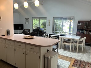 A modern kitchen with a central island, dining area, and a view through large windows. - Rehoboth by the Sea - Ocean Block - 19 Cullen St (Dewey Beach)