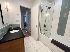 A modern bathroom with a glass-enclosed shower, a sink with a black countertop, and a visible door leading to another room. - Rehoboth by the Sea - Ocean Block - 19 Cullen St (Dewey Beach)