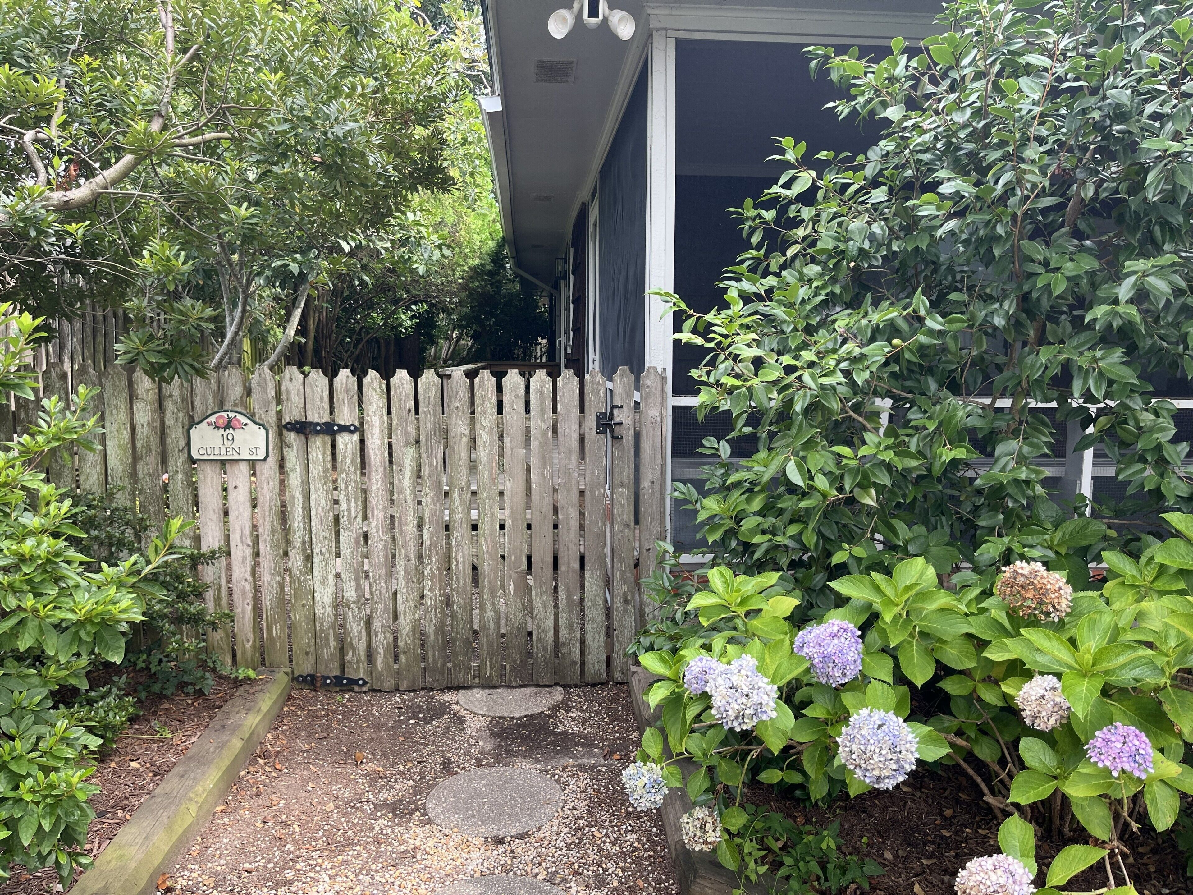 A wooden gate with a sign, a gravel path, and hydrangea bushes.