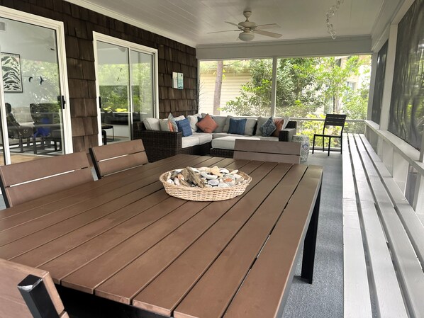 A covered patio with a wooden table, a woven basket, and a sofa with cushions. - Rehoboth by the Sea - Ocean Block - 19 Cullen St (Dewey Beach)