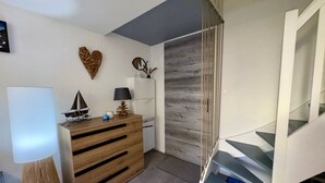 Et moderne værelse med en trækommode, en lampe og et lille bord med dekorative genstande. En trappe med gelænder i glas er synlig.