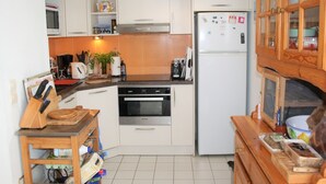 Cocina compacta con armarios blancos, horno empotrado, refrigerador y encimera de madera.