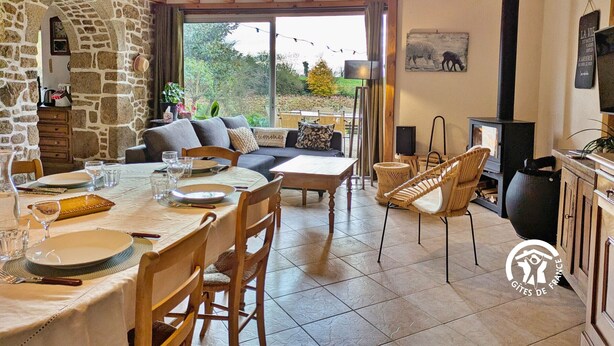 Un coin repas chaleureux avec un mur en pierre, une table en bois dressée pour quatre personnes et des sièges confortables.
