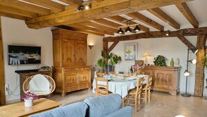 Un salon chaleureux avec un canapé, des meubles en bois, un coin repas avec une table dressée pour quatre personnes et un coin cuisine avec un meuble et des plantes.