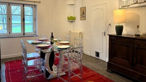 A dining area with a glass table and chairs, a radiator, a lamp, and a view of the outdoors through a window. - Tranquil cottage with SPA, garden and pond, pets allowed for 6 guests (Bézenet)