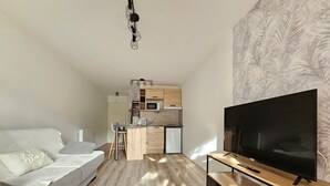Un salon moderne avec un canapé, un téléviseur posé sur un meuble en bois, et une cuisine en arrière-plan.