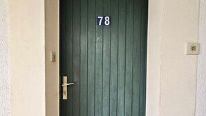 Une porte verte portant le numéro 78, une poignée de porte et un interrupteur sur le mur.