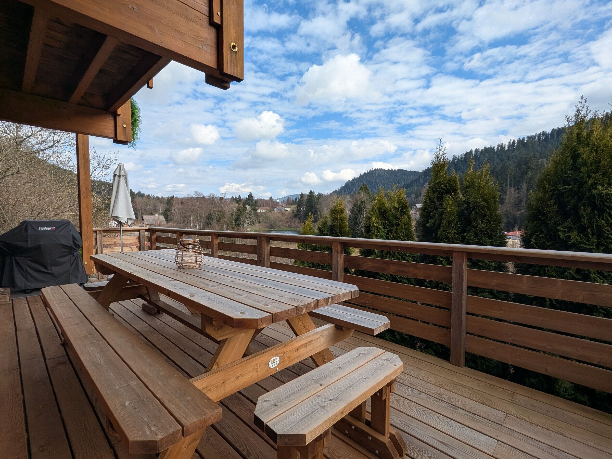 A wooden deck with picnic tables and a grill, overlooking a mountainous landscape.