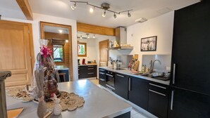 A modern kitchen with a central island, black cabinets, stainless steel appliances, and a wooden ceiling. - Cozy chalet in Gérardmer with spa and sauna (Gérardmer)