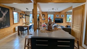 A wooden interior with a kitchen island, dining area, and a living space with a TV. - Cozy chalet in Gérardmer with spa and sauna (Gérardmer)