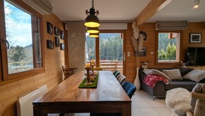 A wooden interior with a dining table, chairs, a sofa, and a TV. - Cozy chalet in Gérardmer with spa and sauna (Gérardmer)
