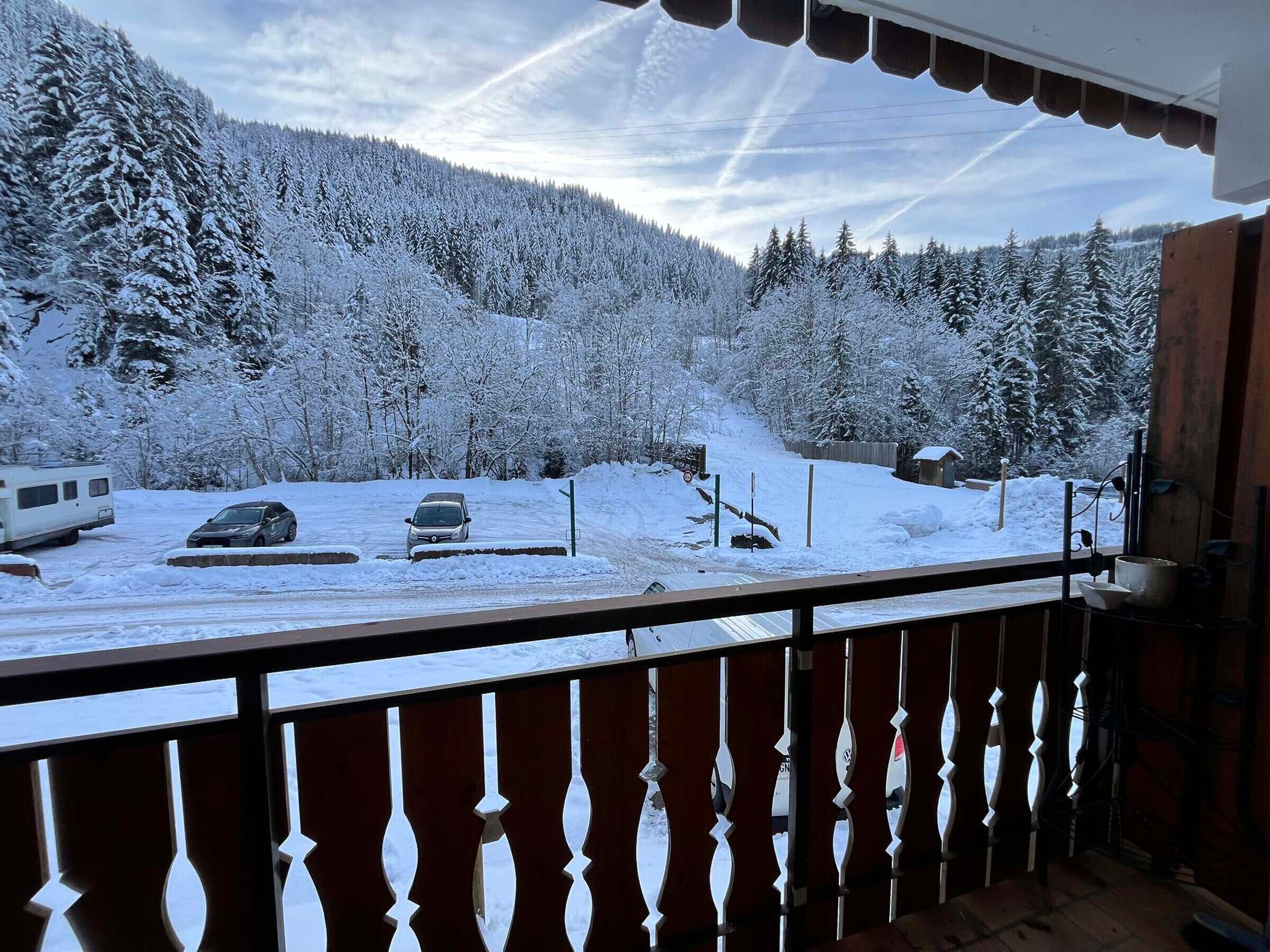 A balcony with a view of a snowy landscape, including a road with parked cars and a trailer.