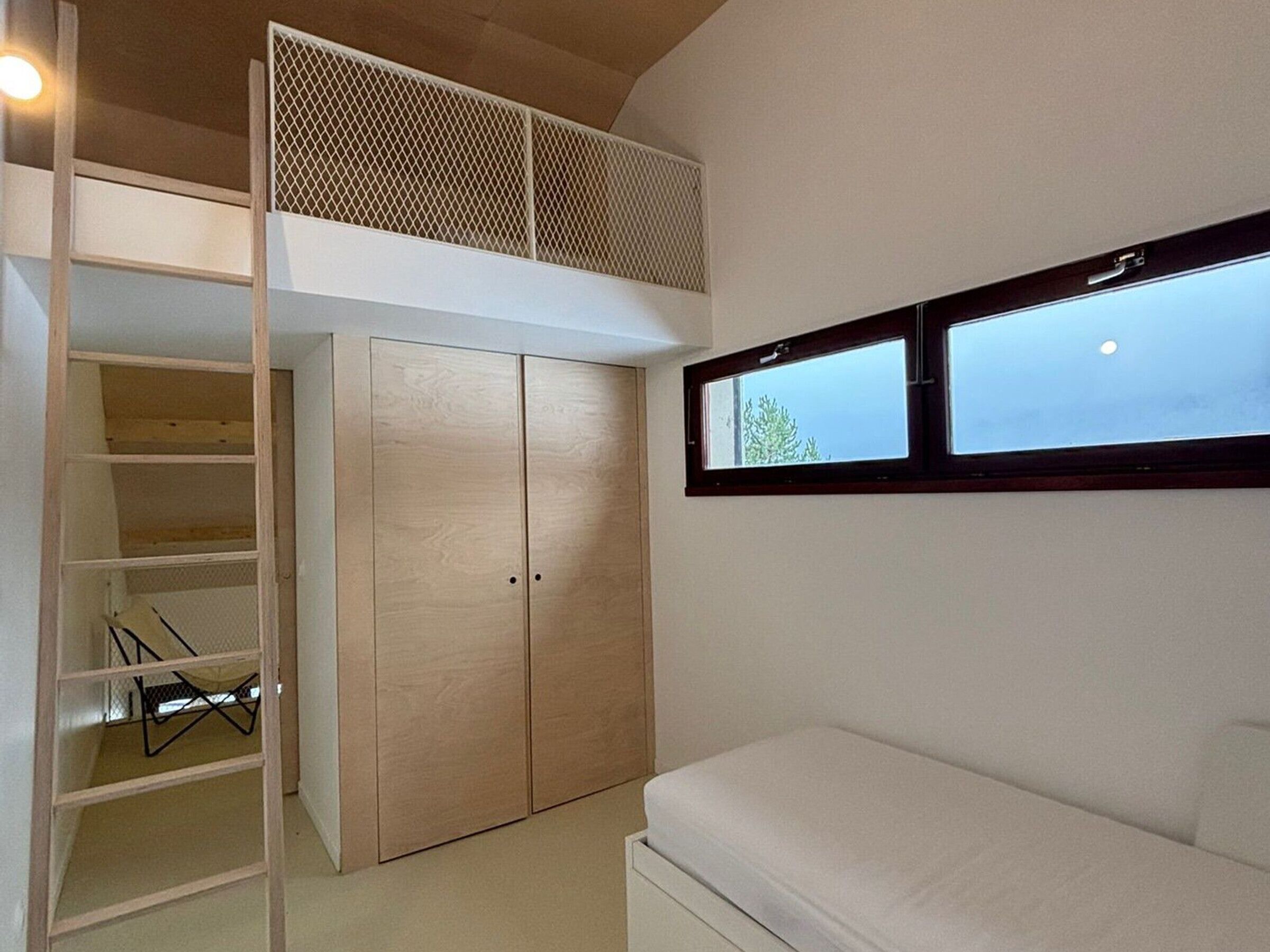 Un dormitorio con cama tipo altillo, armario y ventana.