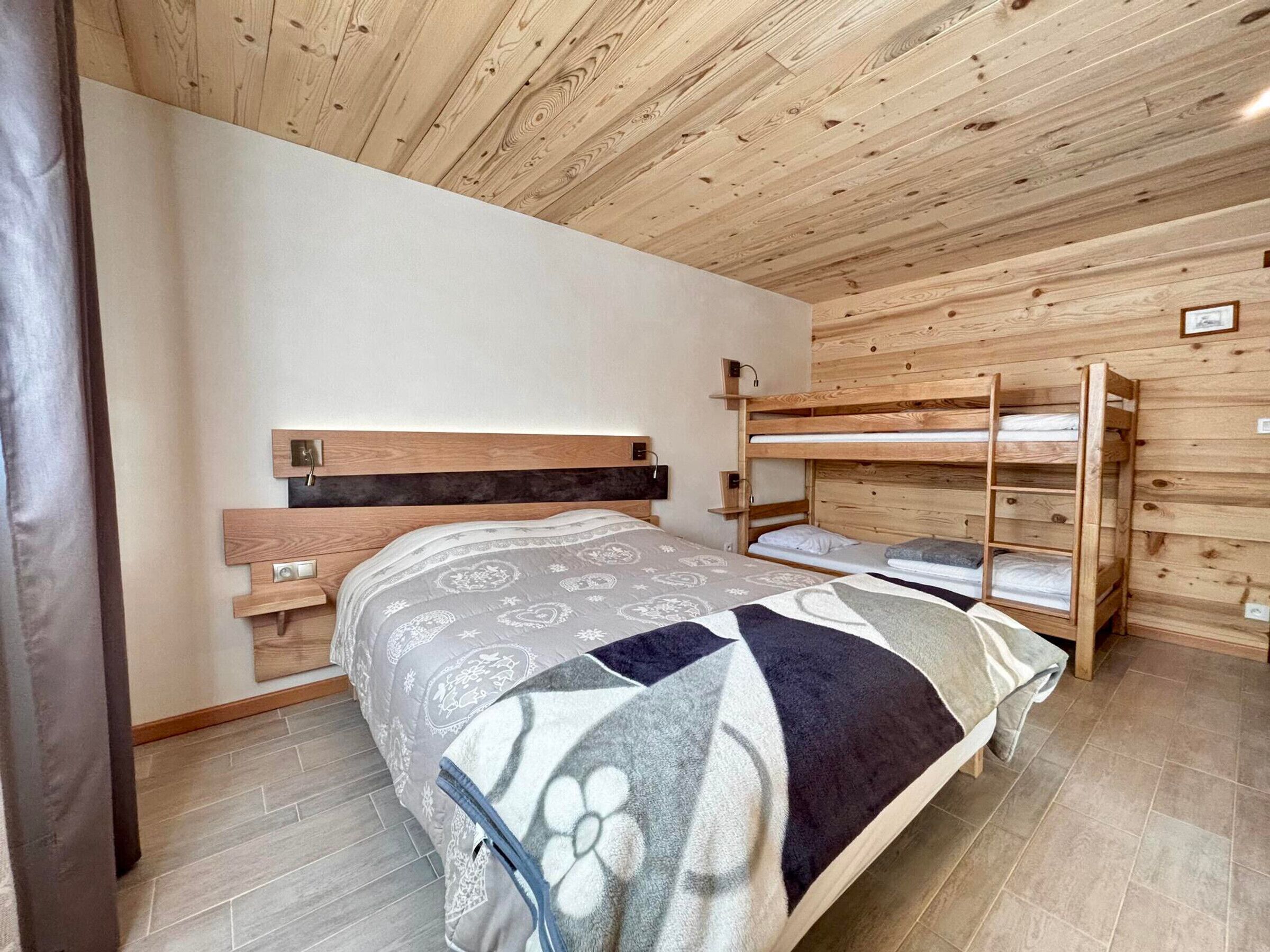 A bunk bed room with a wooden ceiling and walls, a patterned bedspread, and a small bedside table.