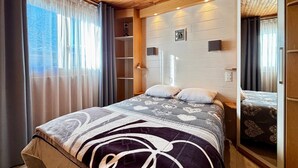 Een slaapkamer met een bed, een kledingkast, een spiegel en een raam met gordijnen.