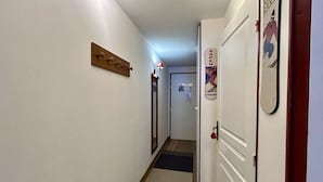 Um corredor estreito com chão de madeira, um porta-roupas e uma porta com um cartaz.