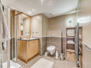 Ein modernes Badezimmer mit einer Duschkabine aus Glas, einem Holzlager für Waschbeckenutensilien, einer Toilette und einem Handtuchhalter.