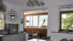 Eine moderne Küche mit einer zentralen Kochinsel, einem Essbereich mit Holztisch und großen Fenstern, die Blick auf Dächer und Grünflächen bieten.