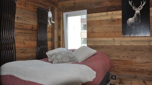 Ein Schlafzimmer mit Holzpaneelen, einem Bett mit rotem und weißem Bezug, zwei Kissen, einer weißen Wanddeko und einem Hirschgemälde.