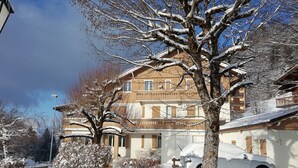Ein zweigeschossiges Gebäude mit Balkon, umgeben von schneebedeckten Bäumen und Büschen.