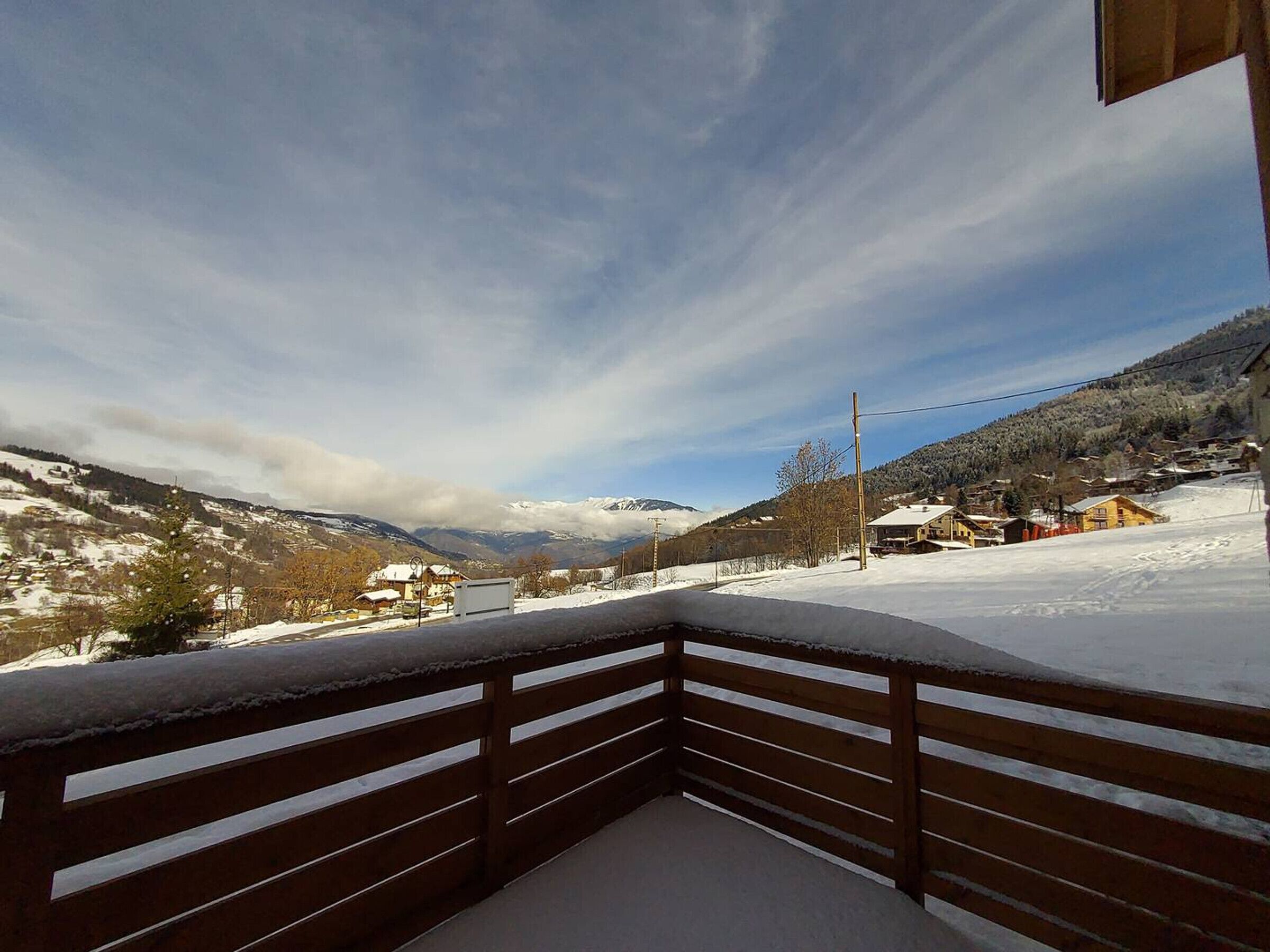 A snow-covered balcony with a view of a mountainous landscape and a village.
