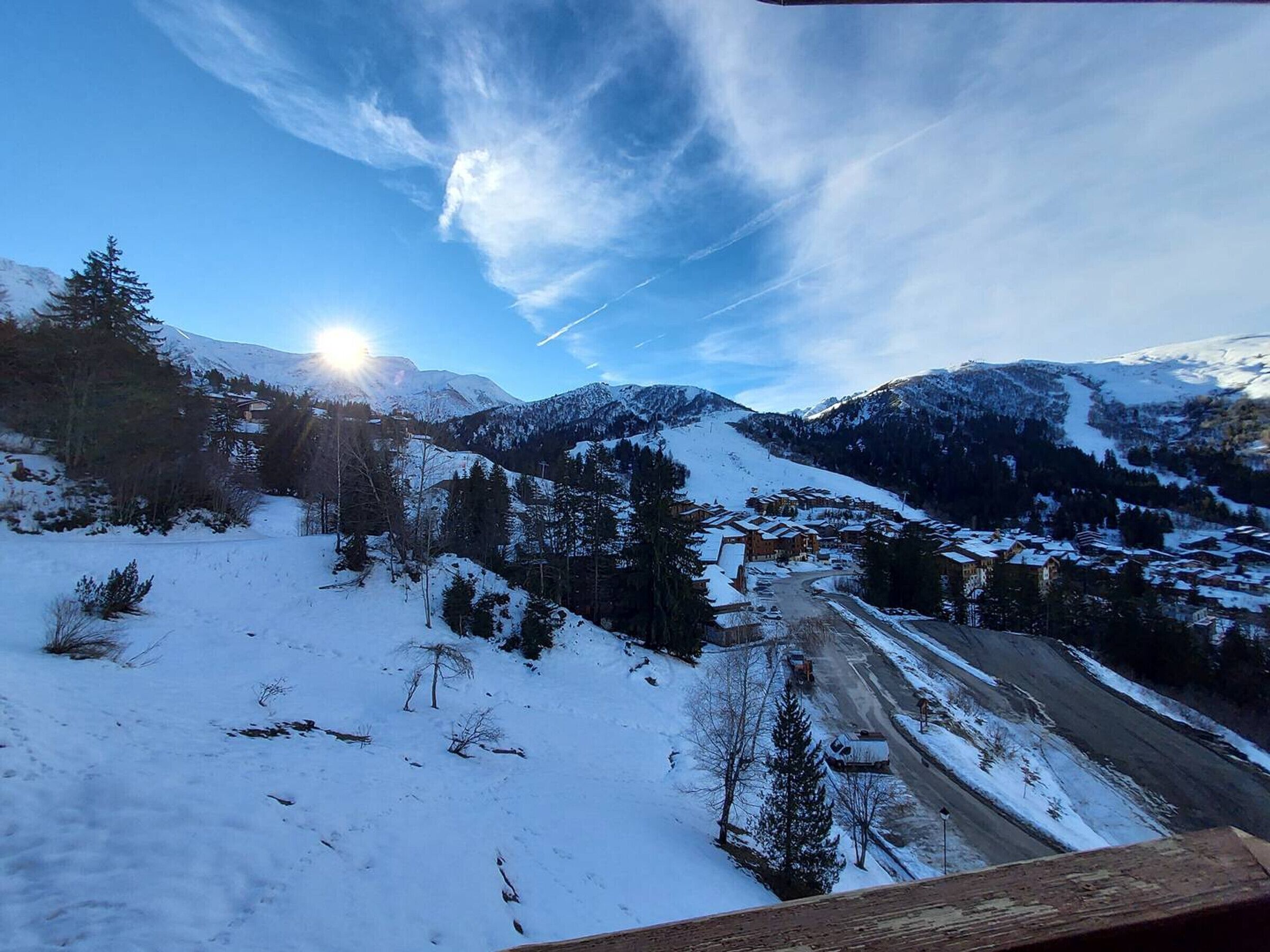 A snowy mountain landscape with a clear sky, a road, and a cluster of buildings.