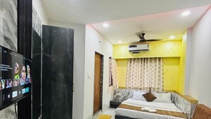A modern bedroom with a bed, a sofa, a TV, and an air conditioning unit. - Hotel G7 (Indore)