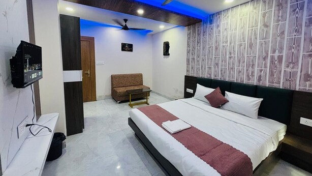 A hotel room with a bed, a TV, a ceiling fan, and a small seating area. - Hotel G7 (Indore)