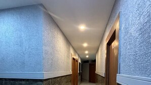 A hallway with marble flooring, textured walls, and wooden doors. - Hotel G7 (Indore)