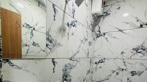 A bathroom with marble walls, a sink, a toilet, and a shower. - Hotel G7 (Indore)