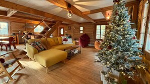L'intérieur d'un chalet confortable, avec un canapé jaune, un fauteuil à bascule en bois, un escalier et un sapin de Noël décoré.