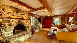 L’intérieur chaleureux d’un chalet en bois avec une cheminée en pierre, un sapin de Noël et un coin salon confortable.
