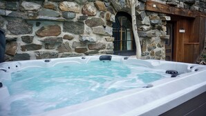 Un bâtiment en pierre avec une porte en bois et un jacuzzi à l’avant.