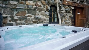 A stone building with a wooden door and a hot tub in front. - Le Vieil Âtre - Rustic chalet & spa (Saint-Jean-Port-Joli)