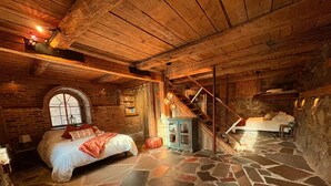 Une chambre à coucher rustique avec un sol en pierre, des poutres en bois, un lit avec des oreillers, une petite table et un escalier.