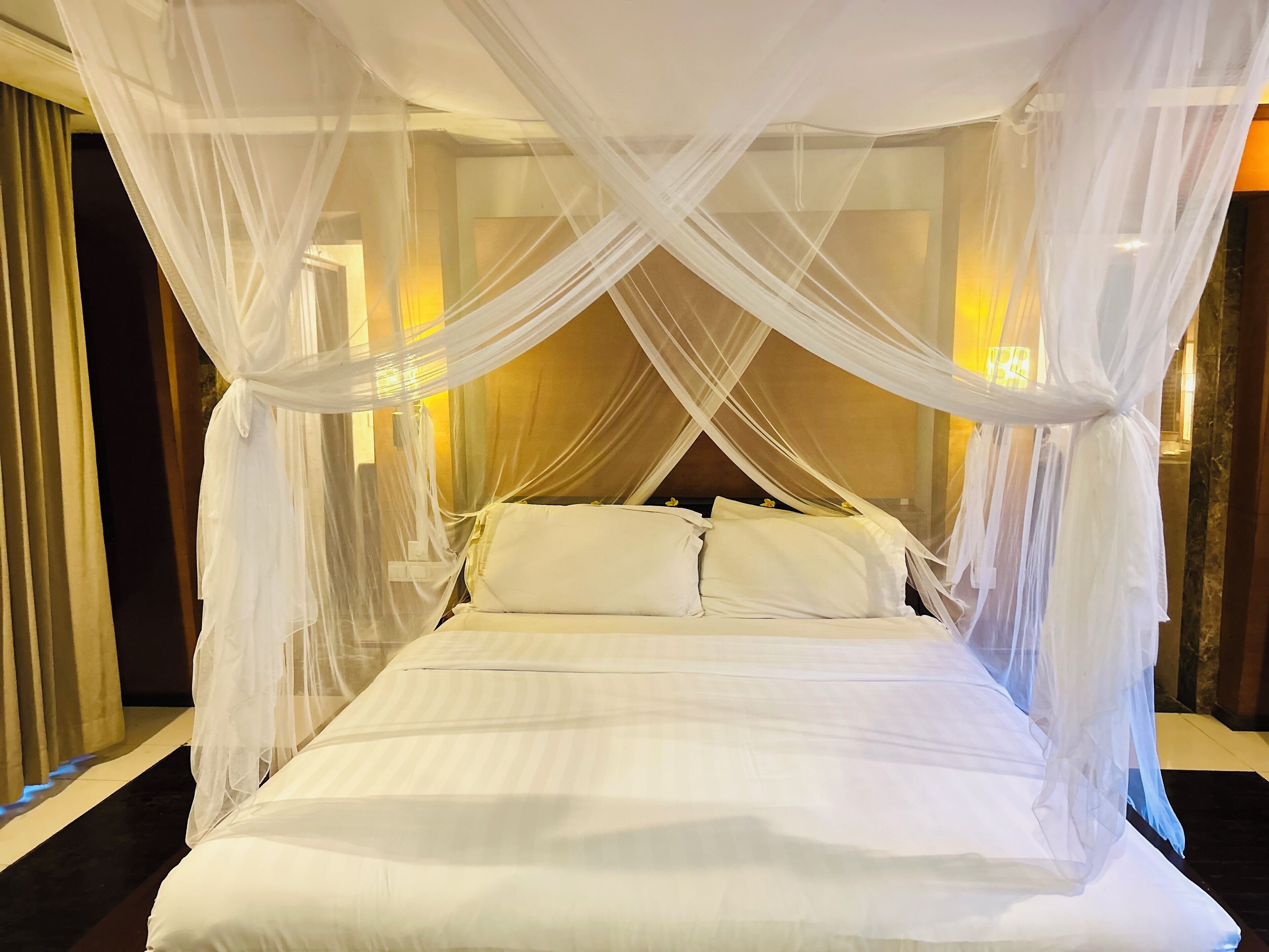 Uma cama com dossel, roupa de cama branca e cabeceira.