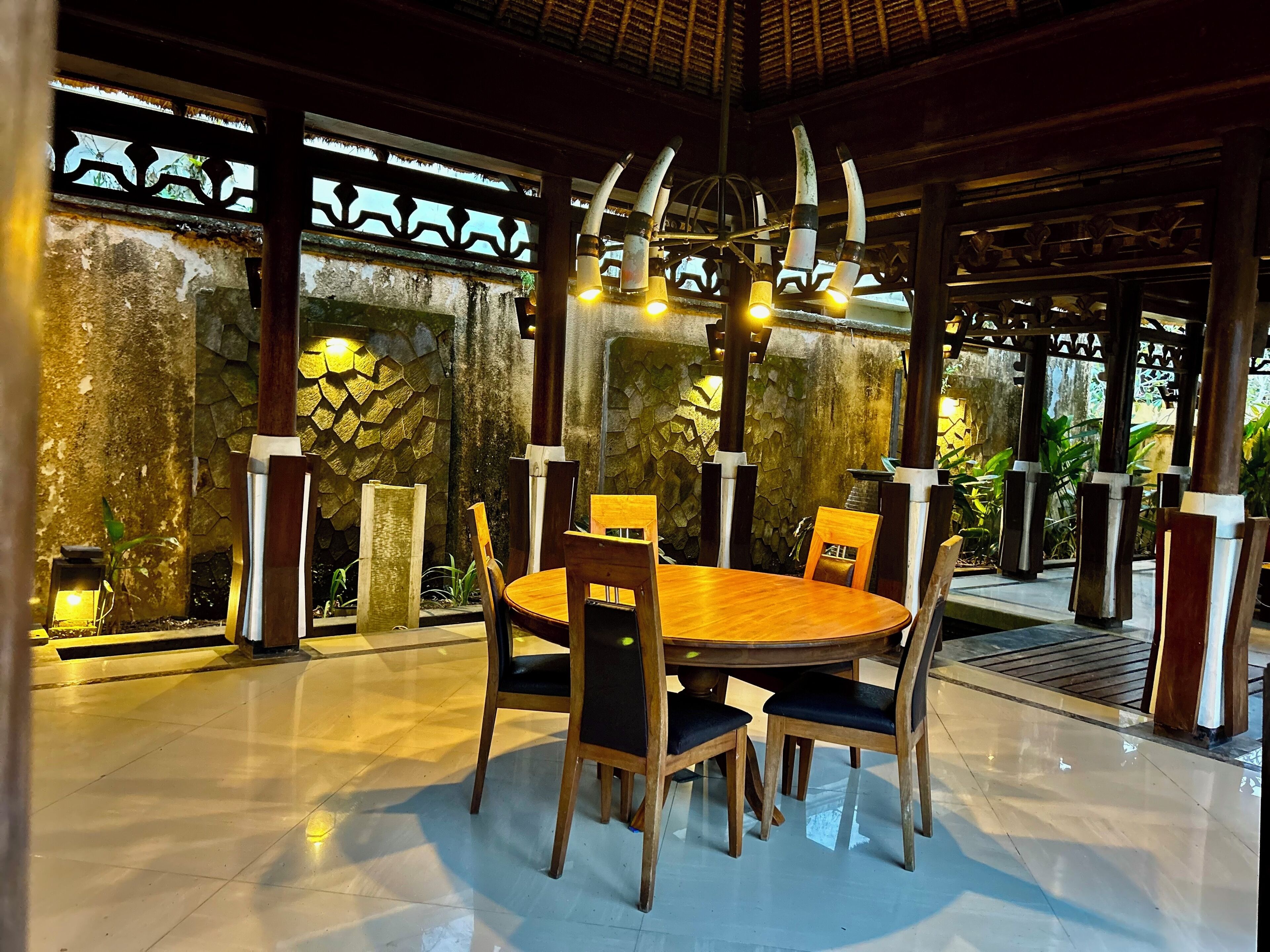 A dining area with a round wooden table and chairs, surrounded by stone walls and a decorative metal fence.