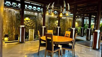 A dining area with a round wooden table and chairs, surrounded by stone walls and a decorative metal fence.