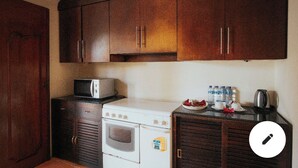 A compact kitchen with wooden cabinets, a microwave, a stove, and a small countertop with bottles and a kettle. - Patmase Villas in Jimbaran (Badung)