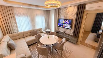 Una sala de estar moderna con un sofá color beige, una mesa de comedor redonda y un televisor montado en la pared.