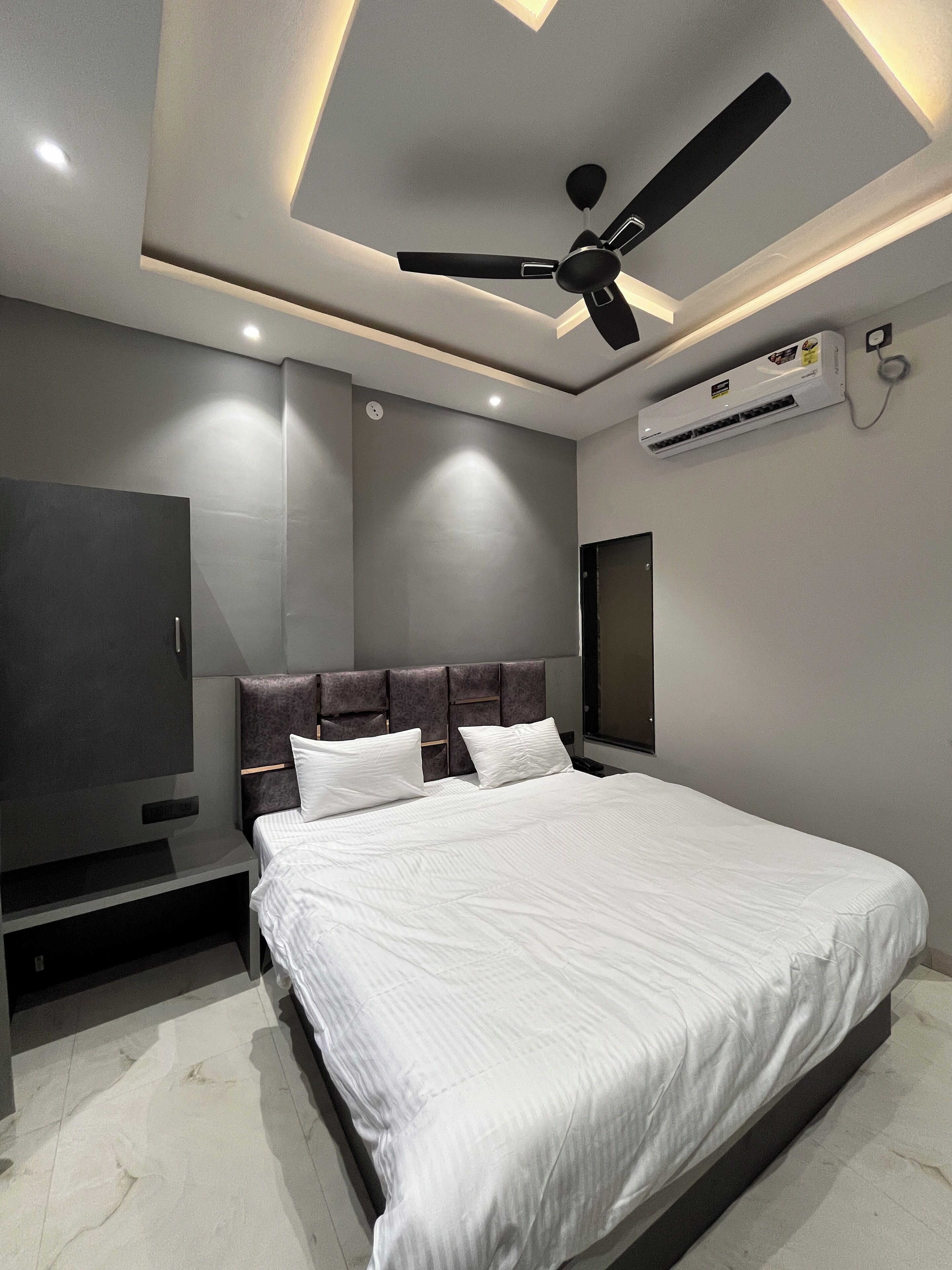 A modern bedroom with a large bed, a ceiling fan, an air conditioning unit, and a flat-screen TV.